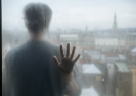Persoon kijkt door beslagen glas als visualisatie van het gevoel van derealisatie